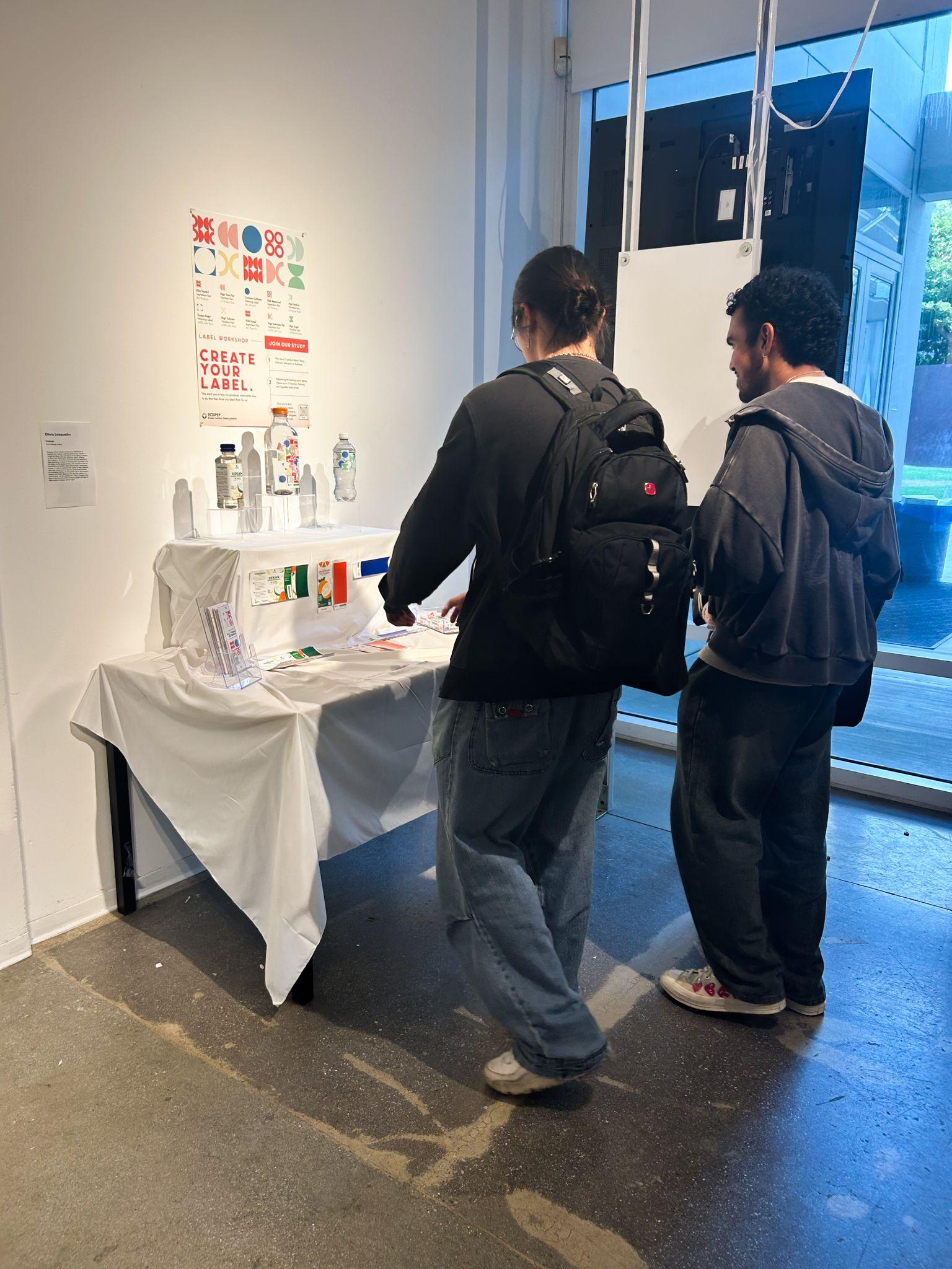 3 visitors stand in front of the Ocispep table, chatting about the products and inspecting the product labels.