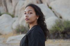 Sadia looks at camera over her shoulder. Large desert rocks and plants form the background.