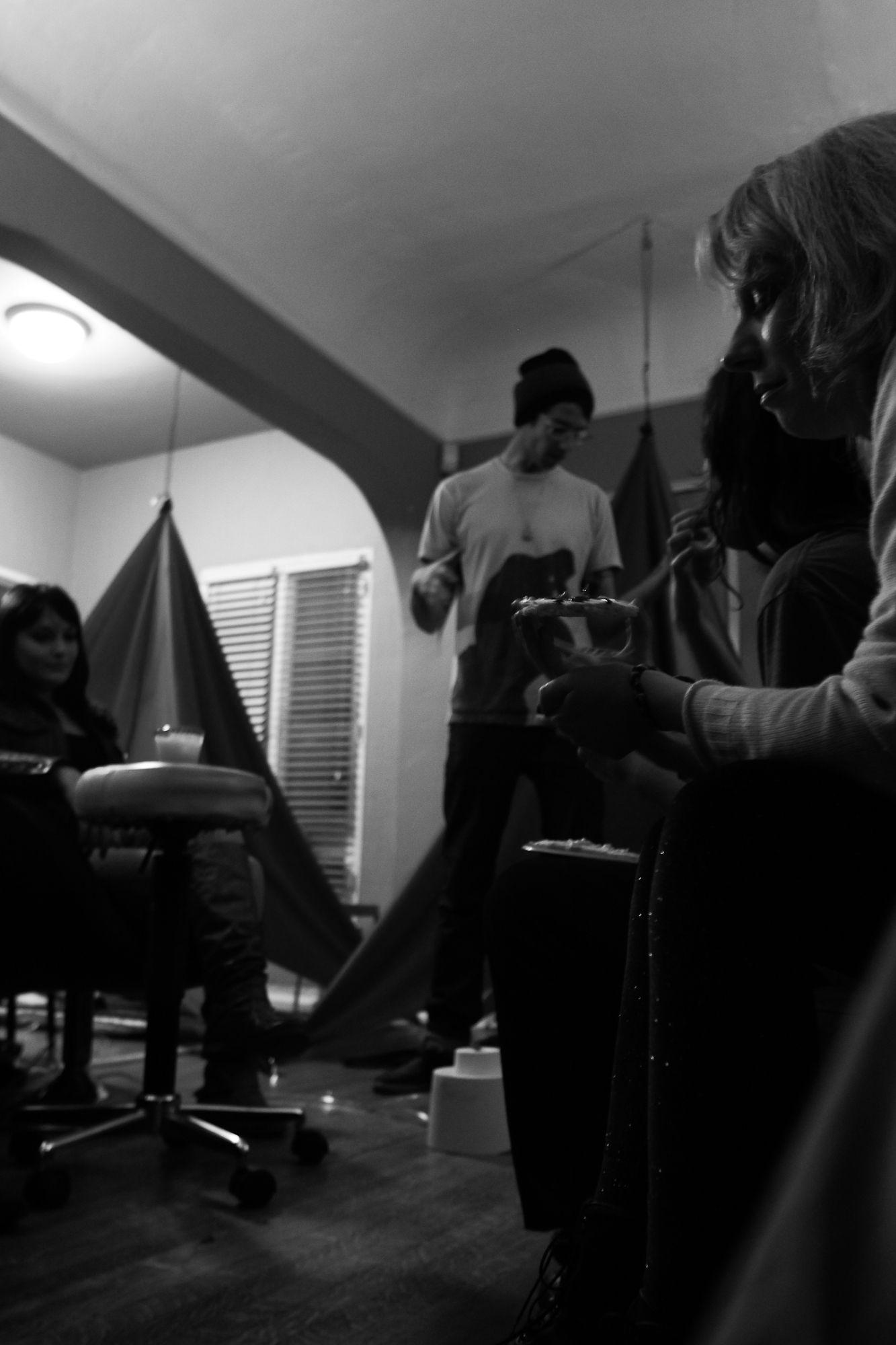 This is a dark grayscale photo of someone holding a drink from the side. In the background, there is a tent, a person standing, and a person sitting.