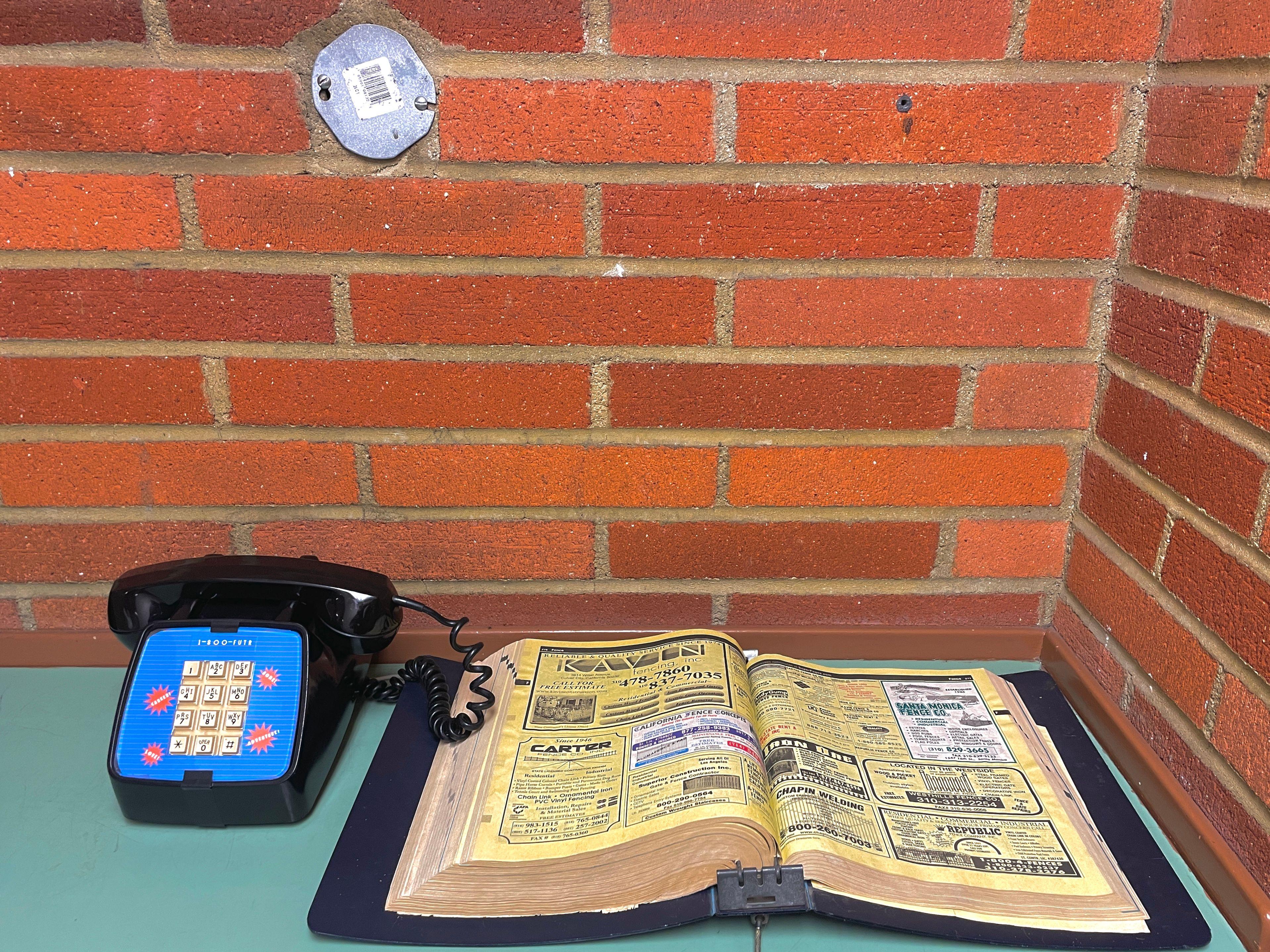 An old touchtone phone next to a brick wall with an old yellow pages phonebook next to it. The phone tells the future.