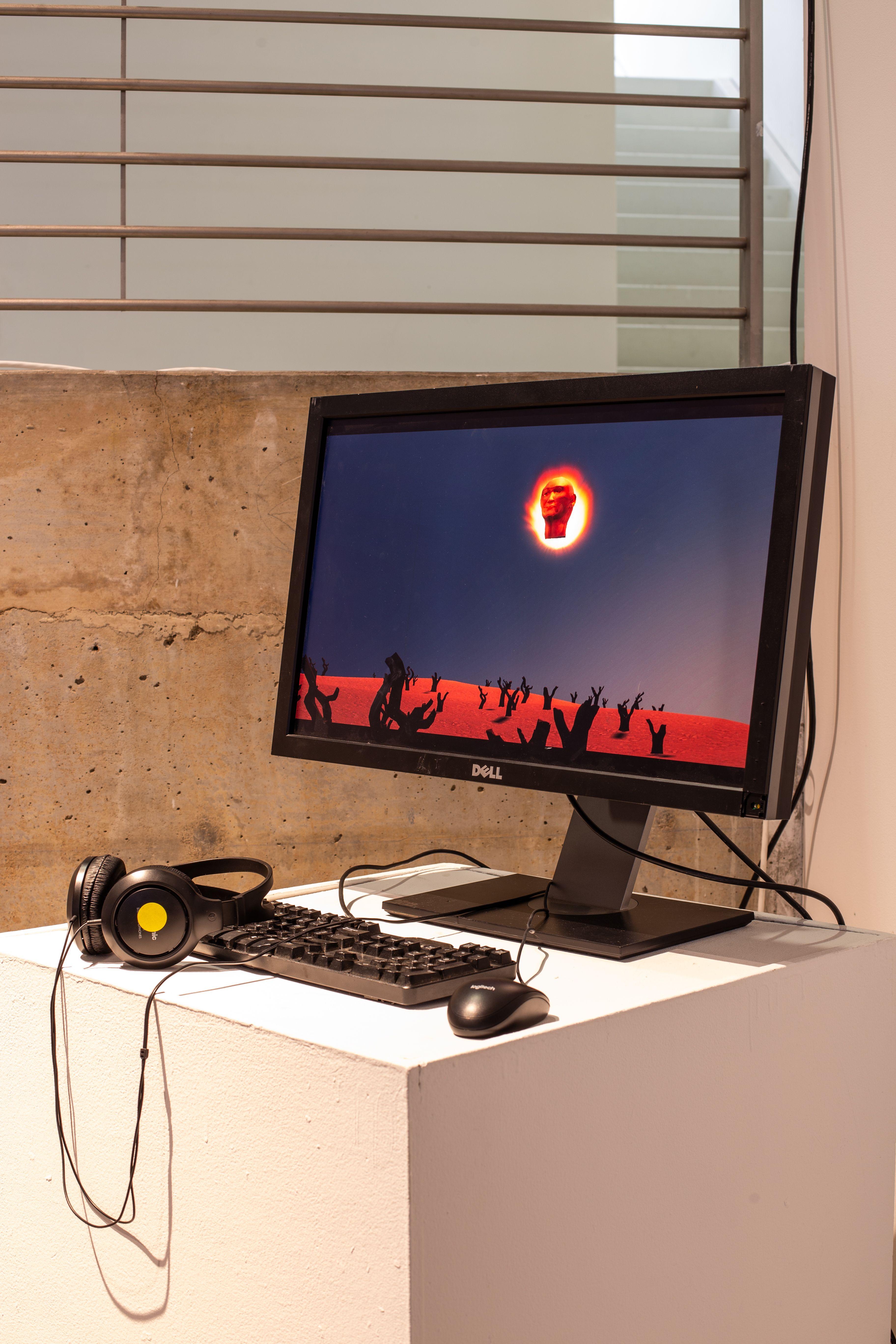 A monitor with a keyboard, mouse and headphones, on which a barren desert landscape with burnt, chopped trees is displayed. Above the desert landscape, a large head floats in front of the sun, illuminated from behind.