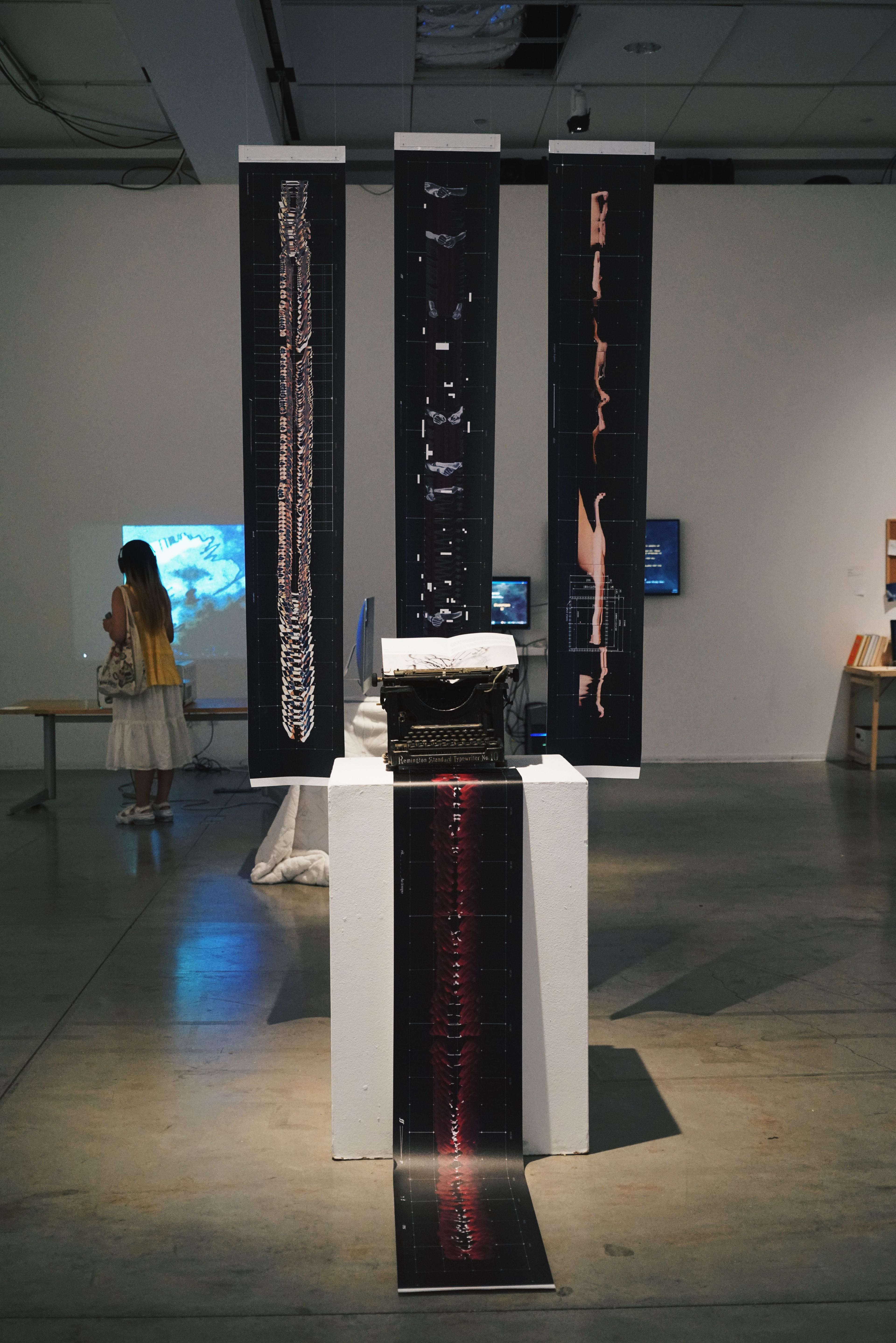 Three banners with abstract, warped forms stand behind a typewriter, from which a similar banner emerges.