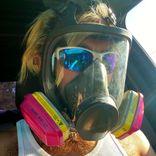 man sitting in a car wearing a gas mask and sunglasses