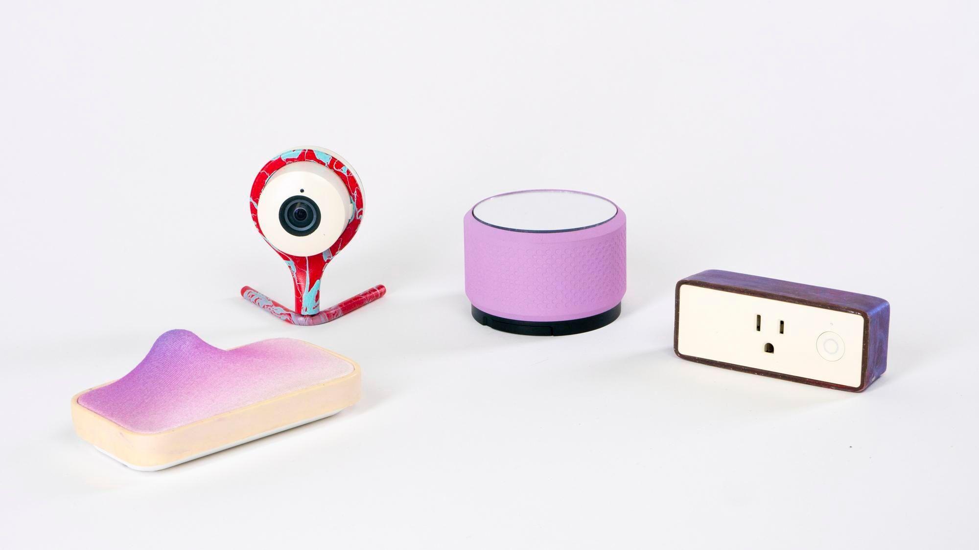 four electronic devices, camera with a cyan and magenta dye colored stand, a purple cylindrical speaker, a purple rectangular outlet and a white to purple gradient rectangular microphone with a lump next to one of the longer edges.  