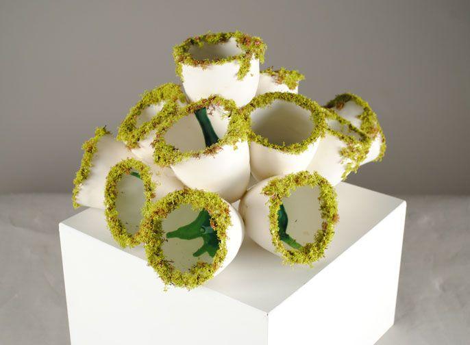 There is a flower bouquet like arrangement of white cup shaped objects. On the rim of all objects is a mossy green kind of material. There are splashes of darker green paint inside the cups.