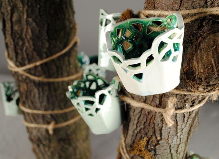 This is a close up of two pieces of wood wrapped with twine and little white baskets. The baskets are connected by the twine and have a white exterior and green interior. The baskets look like they are glossy and made of ceramic.