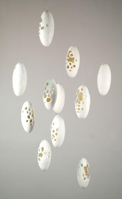 There are 11 white pod like objects suspended from the ceiling, all with lots of holes in them. Each is arranged randomly; some have the holes facing the camera, some do not have any holes visible to the camera.