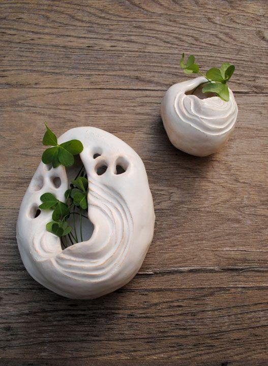 There are two off white ceramic bowl like sculptures. There are sprouts coming out of them. There is a wooden background.